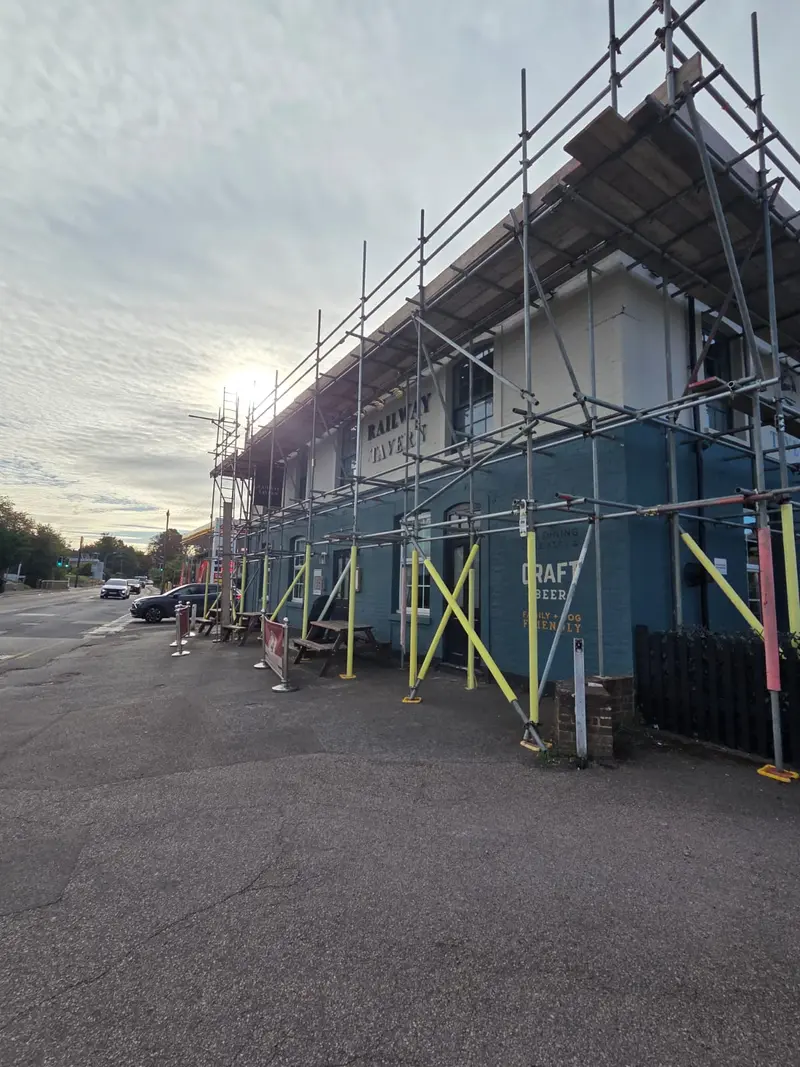 Commercial unit wrapped in independent scaffold at golden hour — tiger-striped base jacks and hoardings visible at ground level